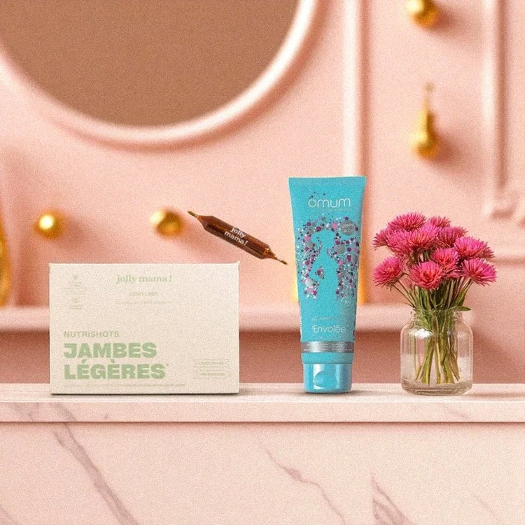 Box jambes légères avec NutriShot Jolly Mama et gel bio Omum Envolée posés sur une étagère rose, accompagnés de fleurs, pour soulager naturellement les jambes lourdes pendant la grossesse et le post-partum