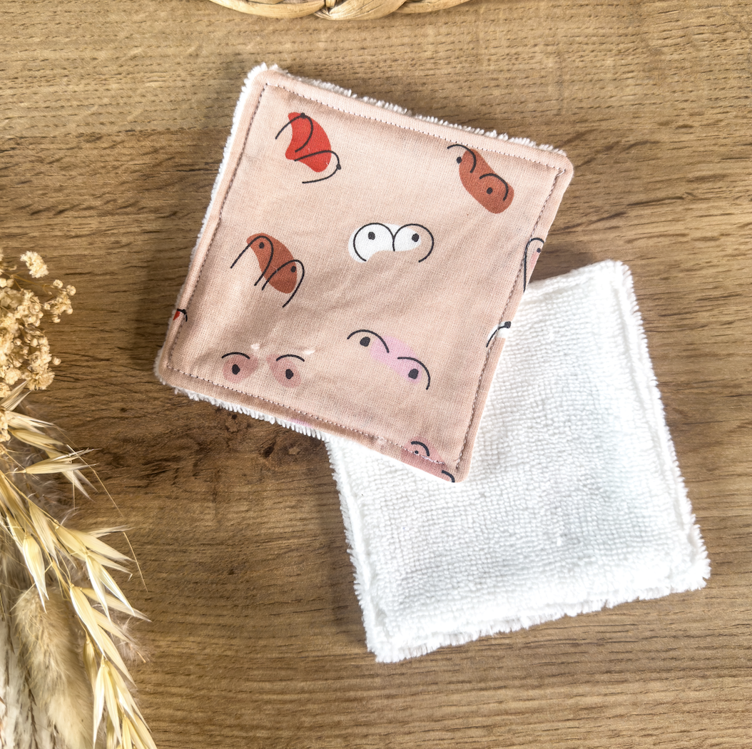 Coton démaquillant réutilisable en fibre de bambou, motif seins, tétons, poitrine, posé sur une table en bois naturel