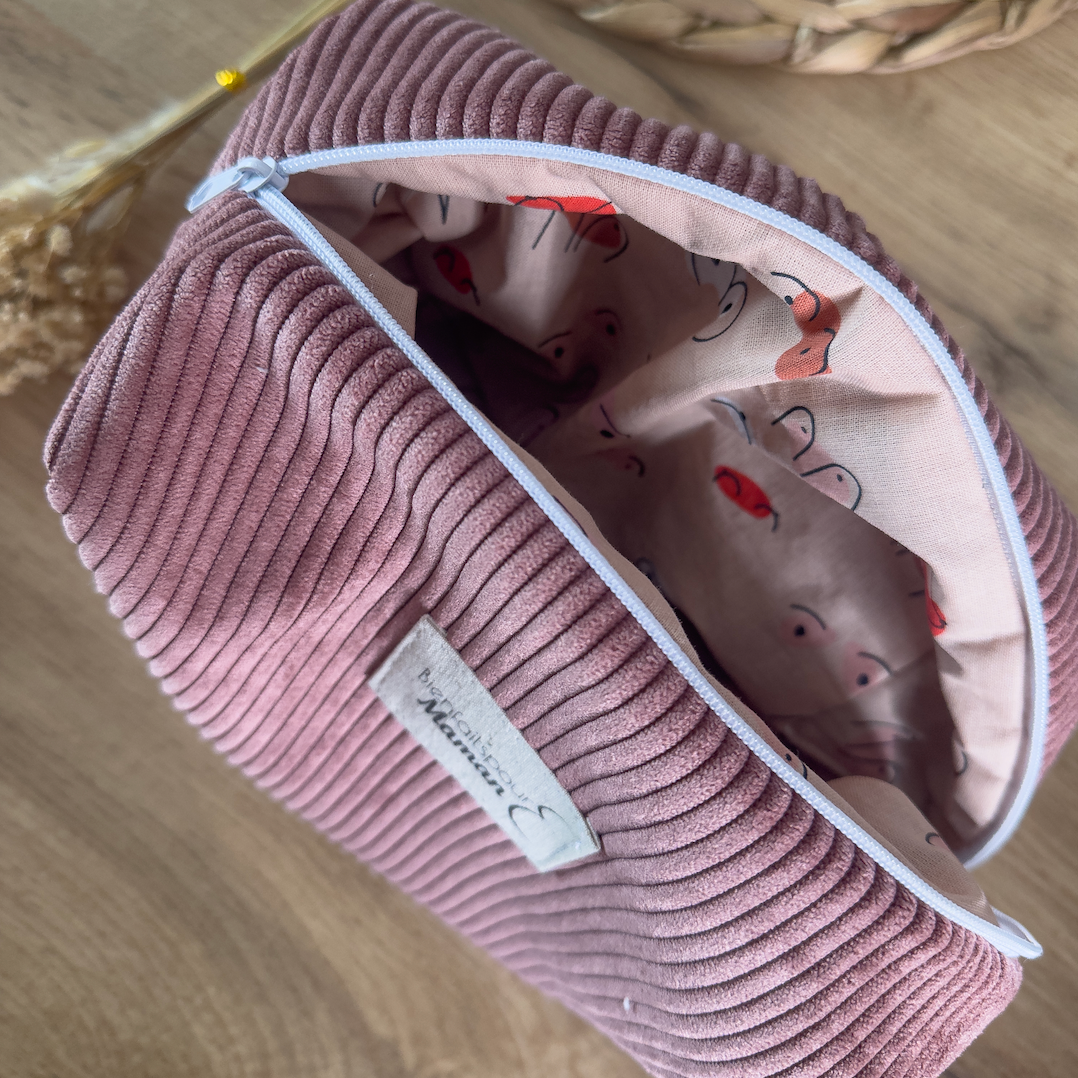 Intérieur de la trousse de toilette en velours rose dévoilant une doublure en tissu à motif ludique pour bébé, avec fermeture zippée.