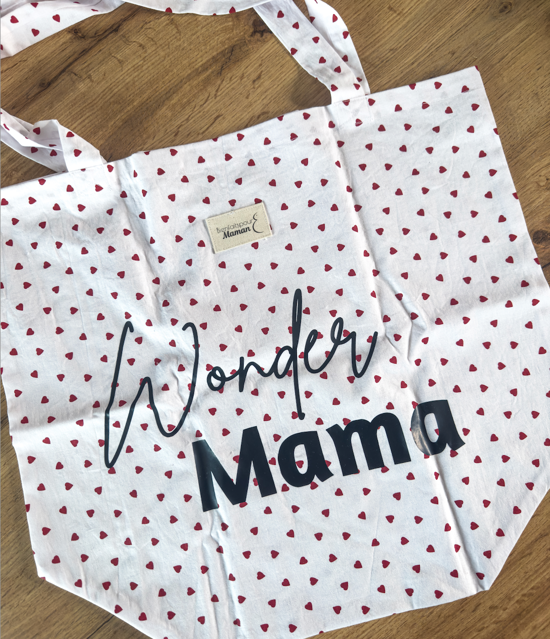 Tote bag à plat sur une table en bois, avec imprimé cœur rouge et message "Wonder Mama" en noir