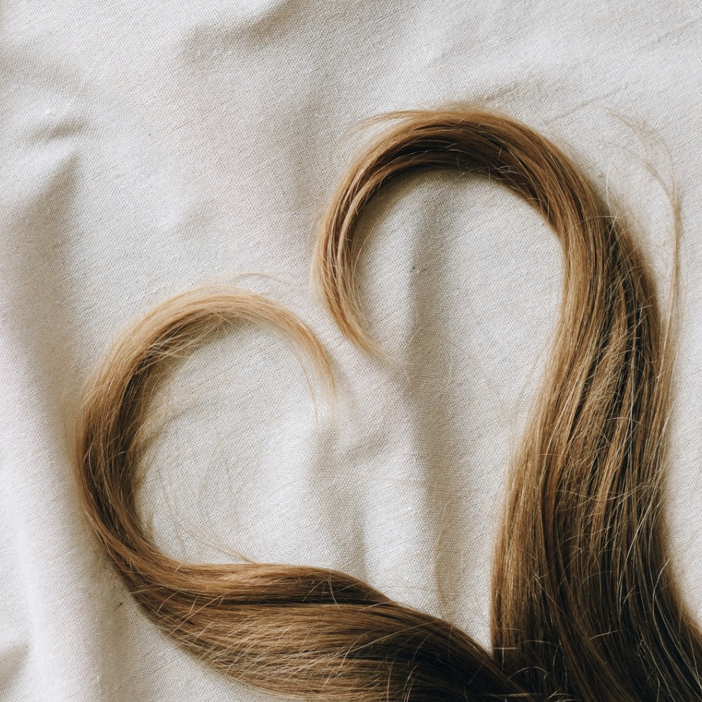 Jeune maman en post-partum qui se regarde dans un miroir en touchant ses cheveux, symbole de chute de cheveux après accouchement.