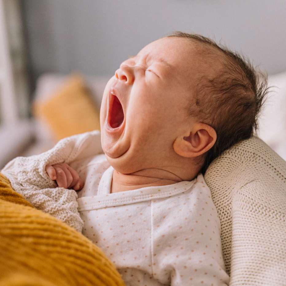  Bébé qui baille dans les bras de sa maman, image illustrant la charge mentale autour du sommeil du nourrisson.