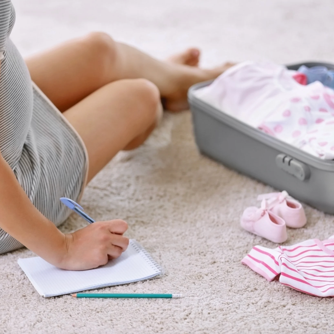 Femme enceinte préparant sa valise maternité avec un carnet de check-list pour l'accouchement — essentiels pour maman et bébé, Bienfaits pour Maman.