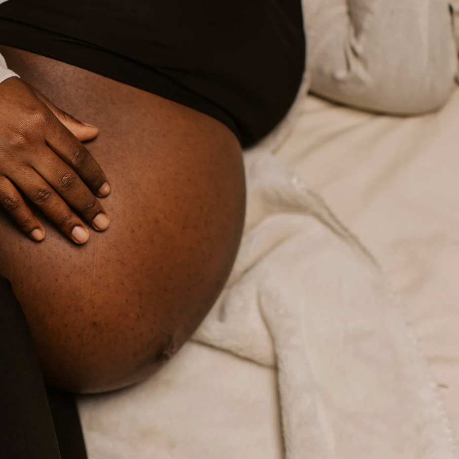 Femme enceinte allongée, main posée sur son ventre, illustrant les évolutions du corps pendant la grossesse, trimestre par trimestre.