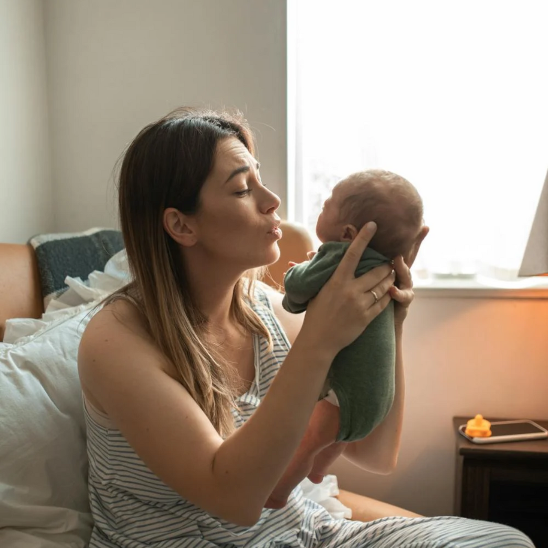 Jeune maman en post-partum tenant son nouveau-né, fatiguée mais remplie d’amour.