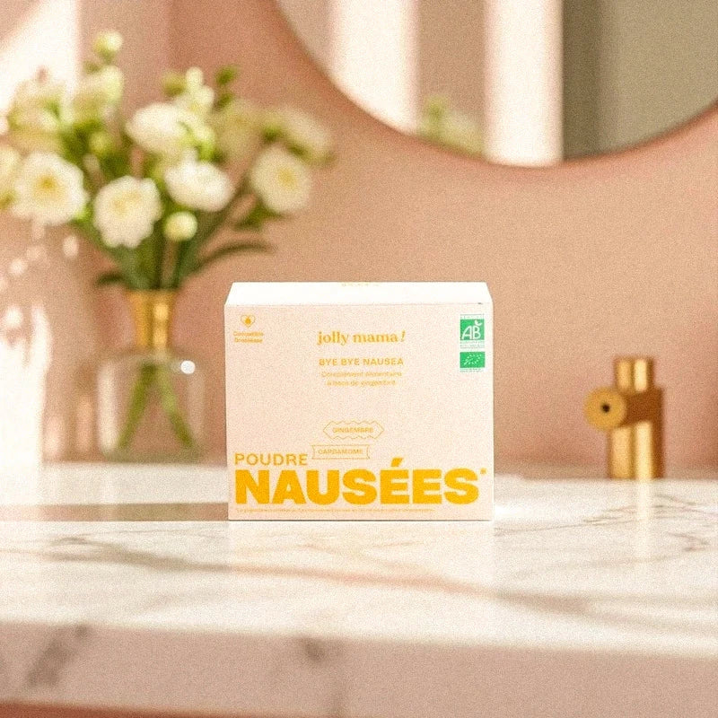 Poudre Nausées Jolly Mama posée sur un plan de travail en marbre avec fleurs blanches en arrière-plan, complément bio contre les nausées de grossesse à base d’ananas et gingembre