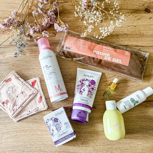 Contenu de la box post-partum Bienfaits Essentiels : poche de gel, soins intimes et corporels bio, brume magnésium, mini huile, lingettes lavables et produits bébé, sur fond bois et fleurs séchées