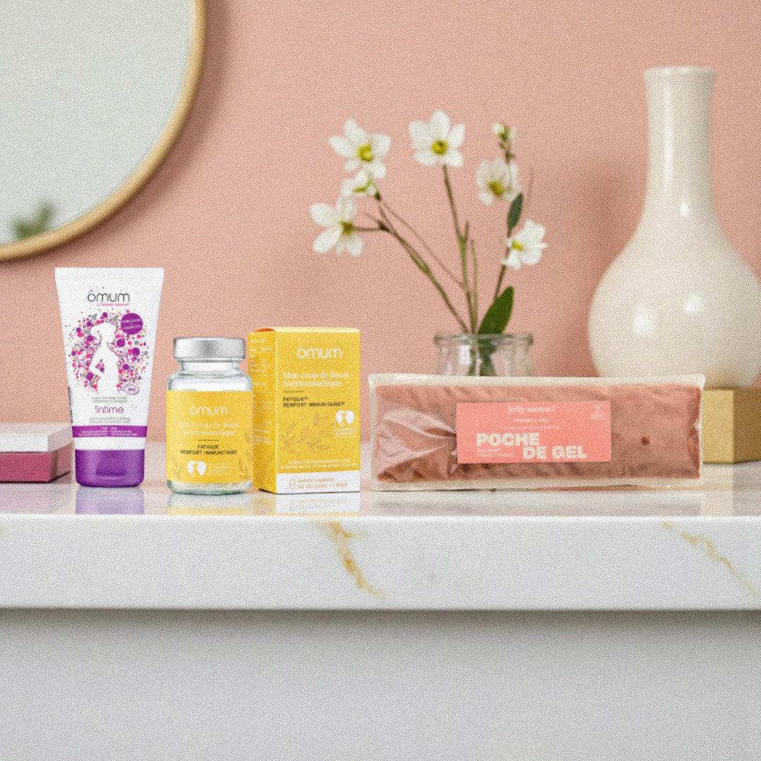 Produits post-partum Omum et poche de gel disposés comme un rituel bien-être dans une ambiance salle de bain chaleureuse. Photo illustrant un coffret de soins naturels pour accompagner la récupération de la jeune maman après l’accouchement.