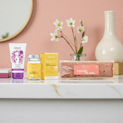 Produits post-partum Omum et poche de gel disposés comme un rituel bien-être dans une ambiance salle de bain chaleureuse. Photo illustrant un coffret de soins naturels pour accompagner la récupération de la jeune maman après l’accouchement.