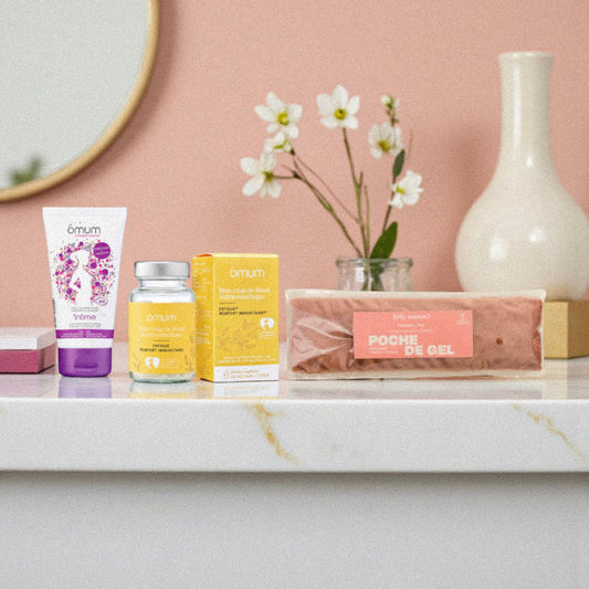 Produits post-partum Omum et poche de gel disposés comme un rituel bien-être dans une ambiance salle de bain chaleureuse. Photo illustrant un coffret de soins naturels pour accompagner la récupération de la jeune maman après l’accouchement.