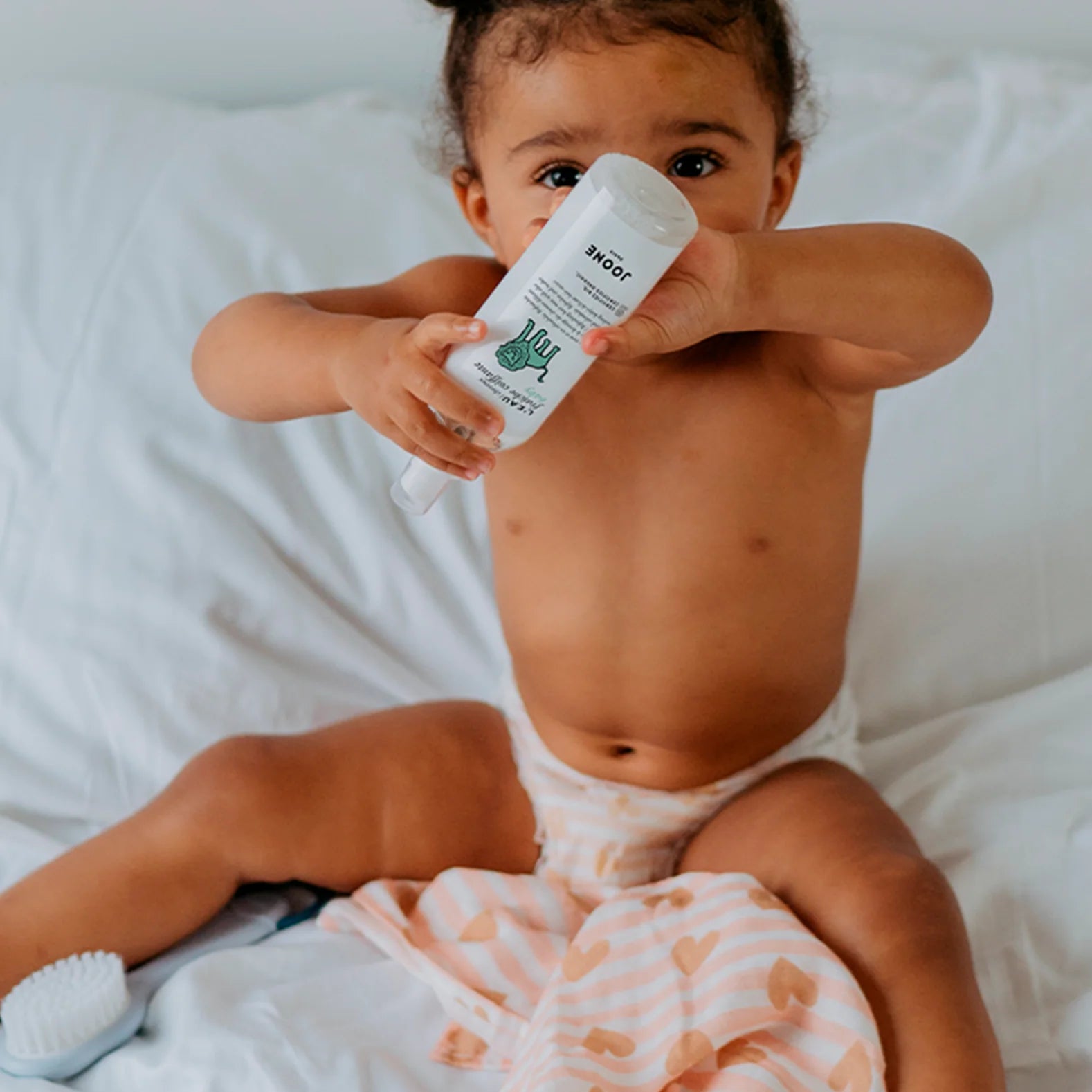 Bébé souriant tenant le flacon d’eau coiffante bio Joone.ire bio et sûr dès la naissance.