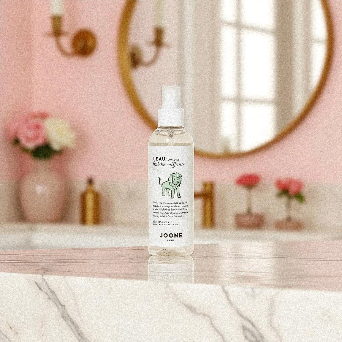 Eau coiffante bio Joone posée sur un meuble de salle de bain au décor rose poudré.