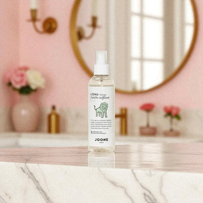 Eau coiffante bio Joone posée sur un meuble de salle de bain au décor rose poudré.