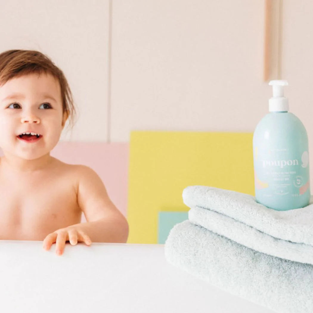 Bébé assis à côté d’un flacon de gel lavant Monjour et d’une serviette, soin hypoallergénique pour peaux sensibles.