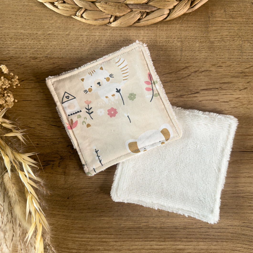 Lingette lavable pour bébé en fibre de bambou avec motif rigolo sur fond rose pâle, posée sur une table en bois