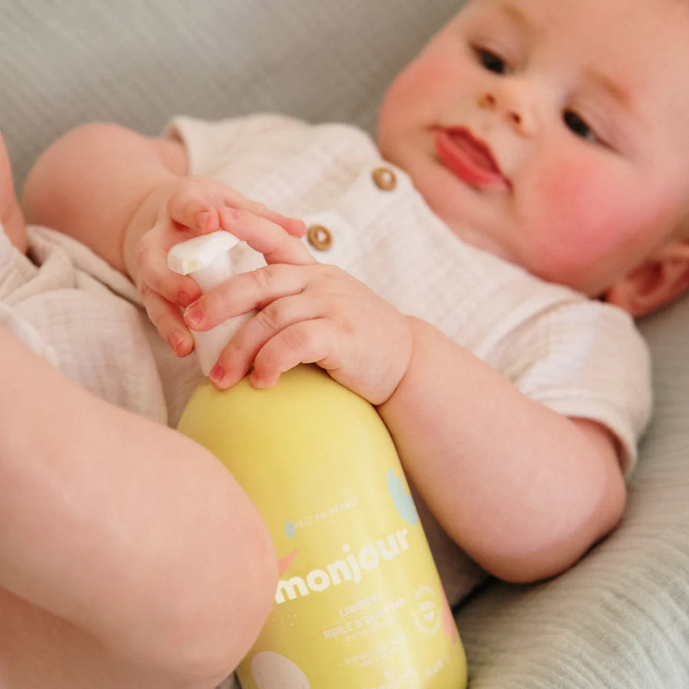 Bébé tenant le flacon jaune de Liniment Oléo-Calcaire Monjour, produit bio nettoyant et protecteur dès la naissance