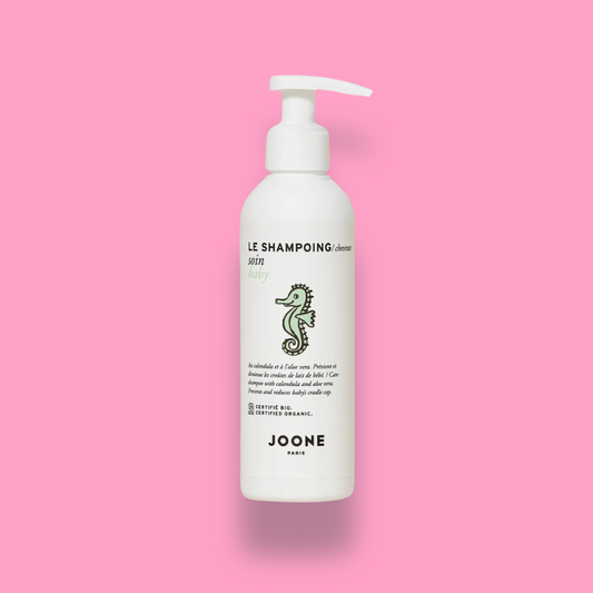 Shampoing bio pour bébé Joone en flacon pompe avec dessin d'un hippocampe sur l'étiquette, sur fond rose.