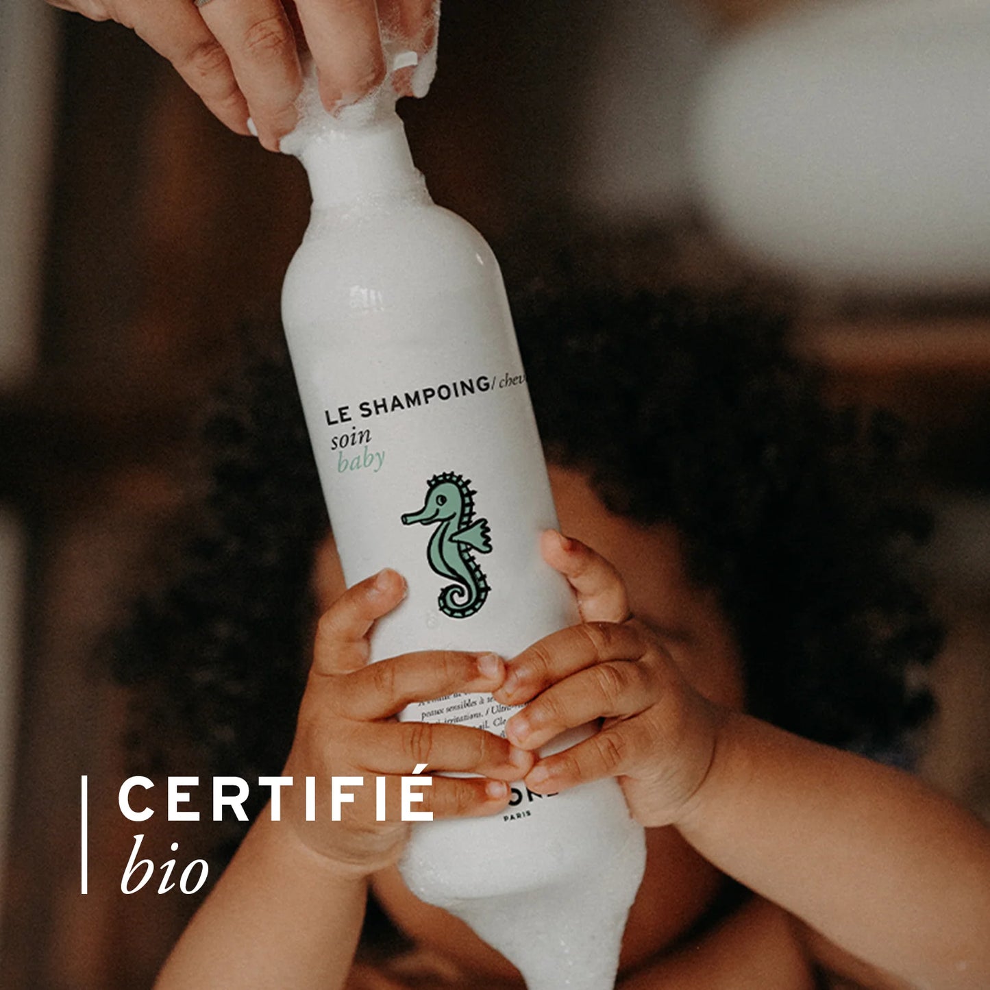 Enfant et parent tenant ensemble le flacon de shampoing soin bio Joone certifié bio.