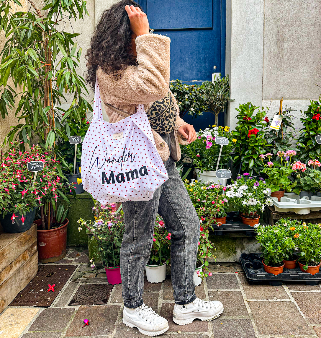  Tote bag blanc à cœurs rouges "Wonder Mama" porté par une femme, devant une boutique de fleurs