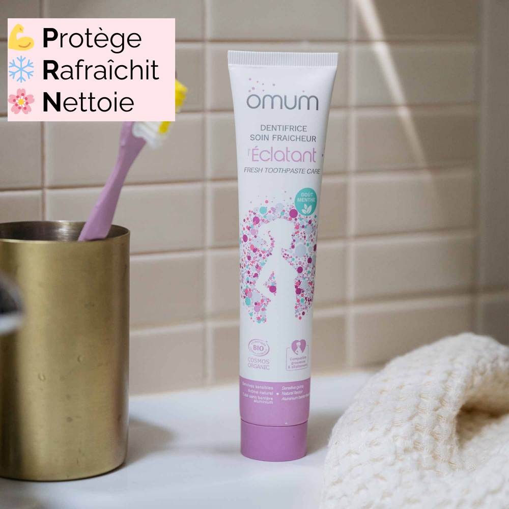 Dentifrice L’Éclatant Omum dans une salle de bain avec brosse à dents, adapté aux femmes enceintes et allaitantes, pour une sensation de fraîcheur et de propreté.