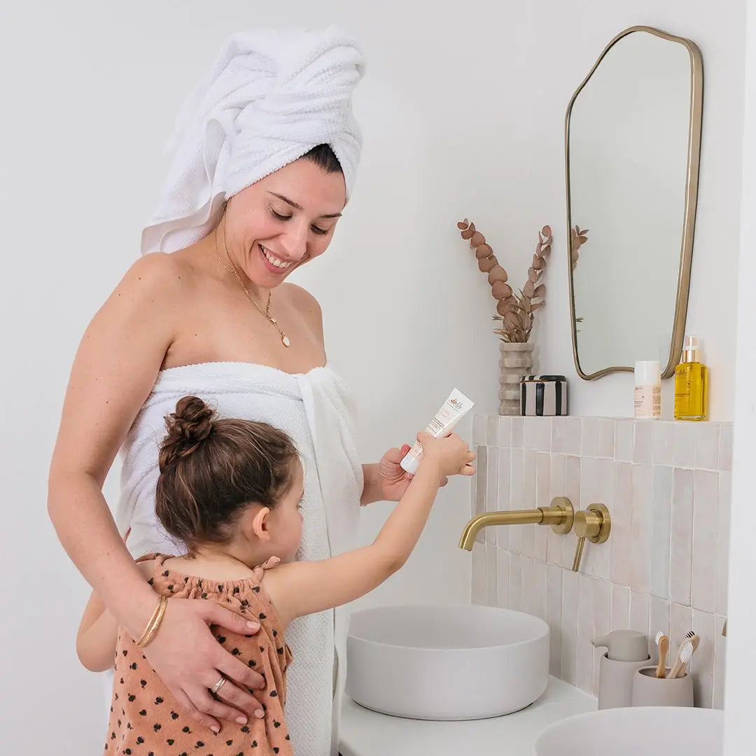 Maman appliquant crème solaire compatible grossesse et allaitement dans salle de bain
